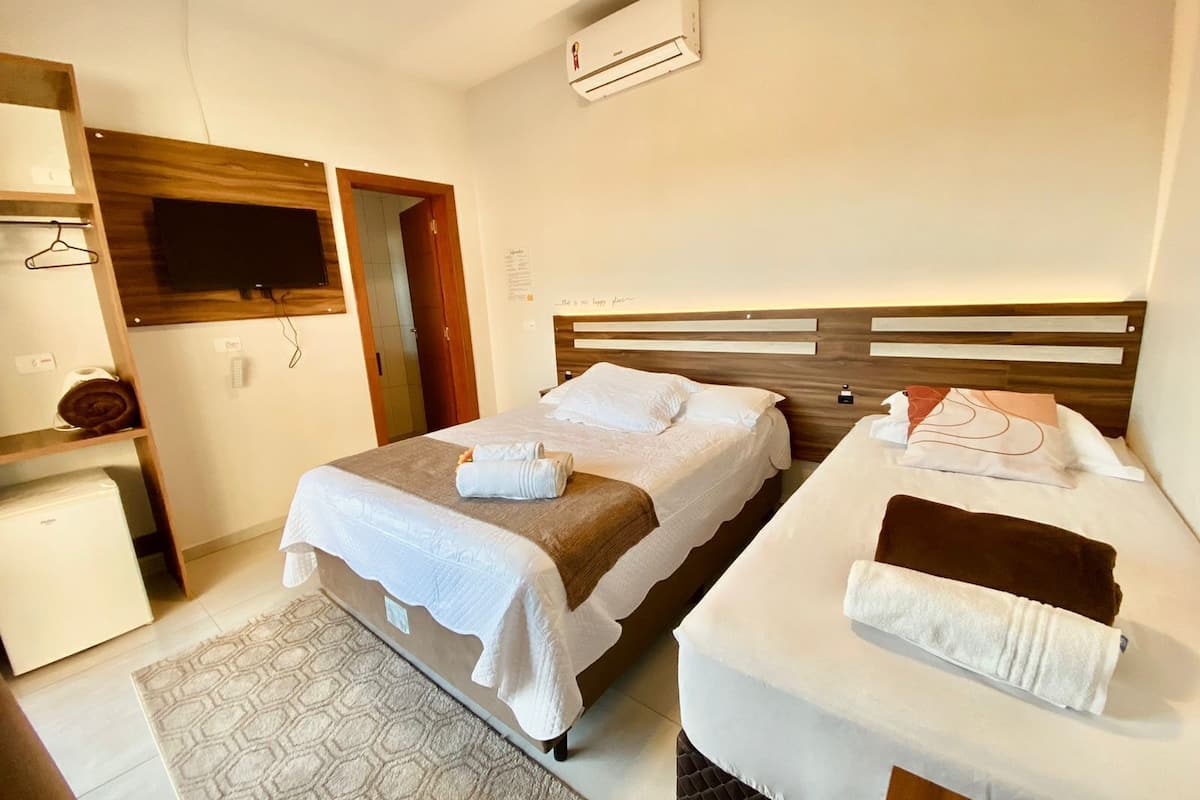 A hotel room with two beds, a TV, a desk, and an air conditioning unit.