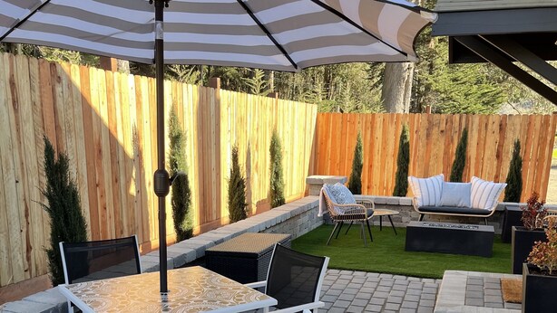 Un patio con mesa y sillas, un paraguas a rayas y una valla de madera al fondo.