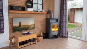Ein Wohnzimmer mit Backsteinwand, einem Fernseher, einem Kamin und einer Schiebetür zum Außenbereich.