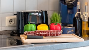 Eine Küchenarbeitsplatte mit einem Toaster, einem Schneidebrett mit einer Wurst und bunten Paprika.