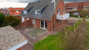 Ein zweistöckiges Haus mit geneigtem Dach, einem Balkon und einer gepflasterten Terrasse.