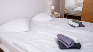 Ein Hotelzimmer mit zwei Betten, weißen Leinentüchern, einem Nachttisch mit Lampe und einem Spiegel, der den Raum widerspiegelt.