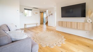 Una sala de estar moderna con un sofá gris, un televisor de pantalla plana grande, piso de madera y un tapete redondo tejido.