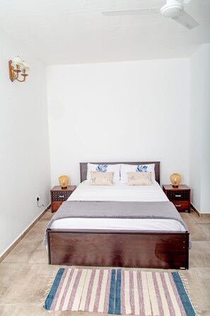 A bedroom with a wooden bed, two nightstands, a ceiling fan, and a wall-mounted light fixture.