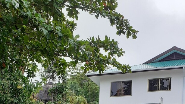 A waterfall flowing over rocks with lush greenery and a white building with a blue roof in the background. - 2-Bed Apt, Sleeps 4, near Beau Vallon Beach (Mahe)