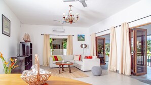 A modern living room with a sofa, a wooden coffee table, a chandelier, and a television. - 2-Bed Apt, Sleeps 4, near Beau Vallon Beach (Mahe)