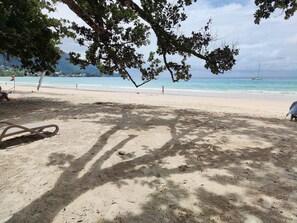 A beach with a clear view of the ocean, a sandy area with shadows, and a few people in the distance.