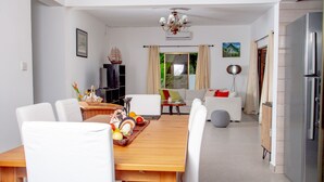 A modern living room with a wooden dining table, white chairs, a sofa, and a television. - 2-Bed Apt, Sleeps 4, near Beau Vallon Beach (Mahe)