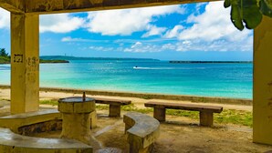 Blick von einer überdachten Terrasse auf einen Strand mit Bänken und blauem Himmel.