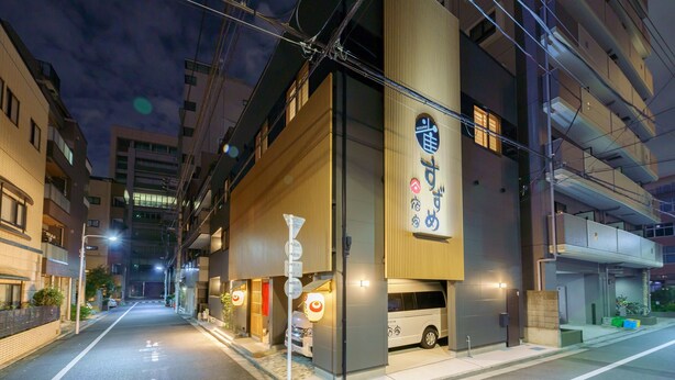 A modern building with a prominent sign, a vehicle parked outside, and a clear street. - Yadoya Suzume (Tokyo)