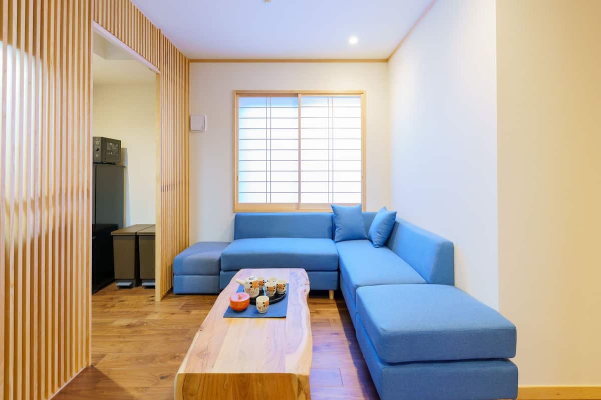 A modern living room with a sectional sofa, a wooden coffee table with decorative items, and a large window with blinds.