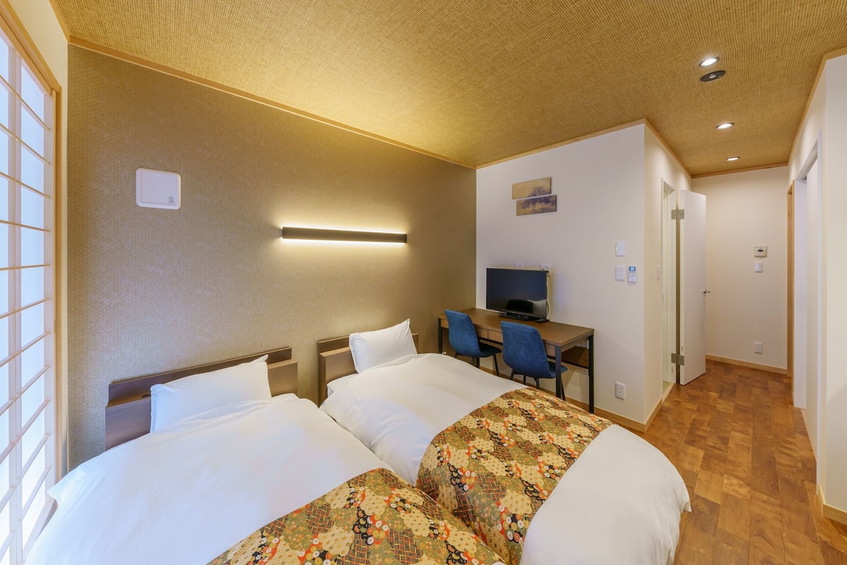A hotel room with two beds, a desk, a television, and a bathroom door.
