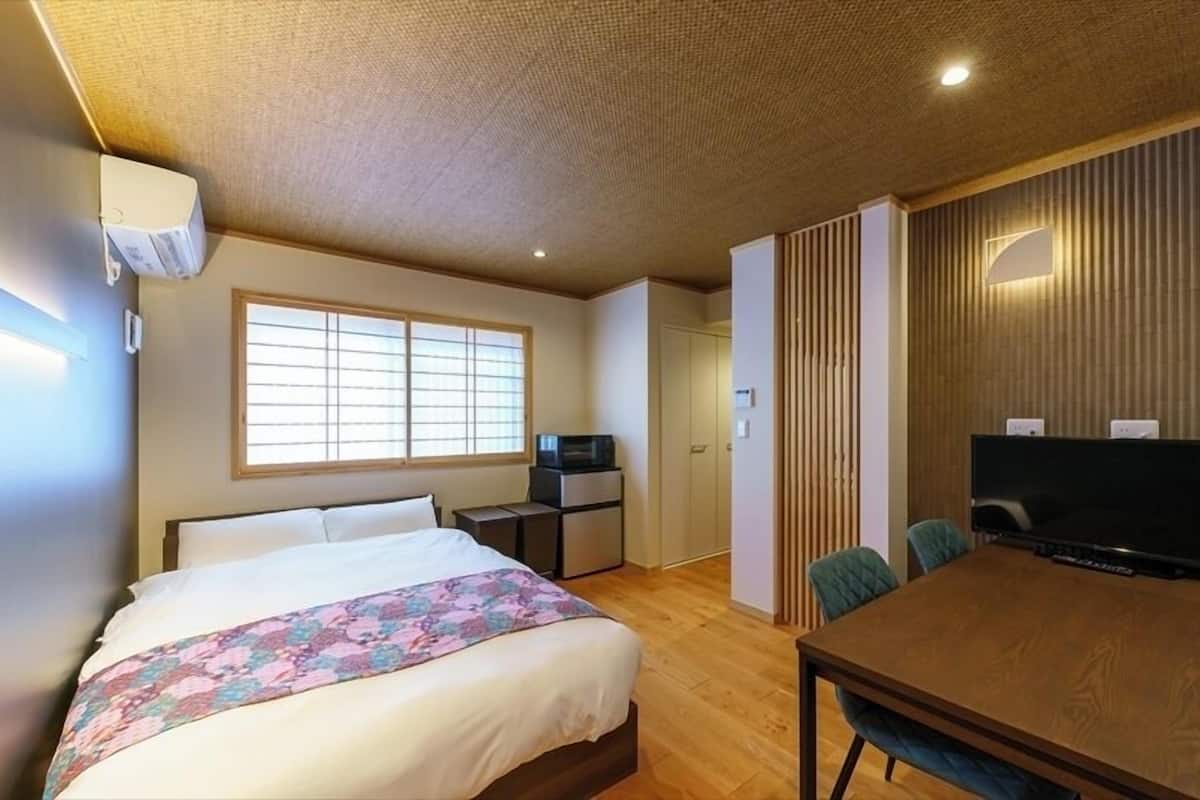 A hotel room with a bed, a desk with a computer, a television, and a dining table with chairs.