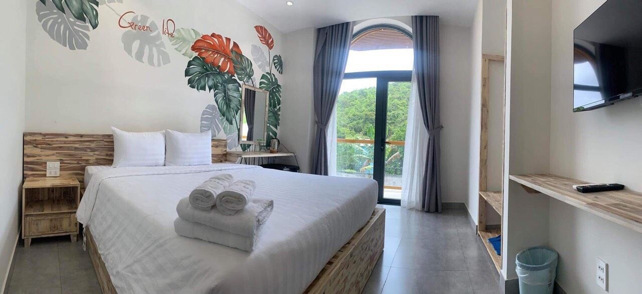 A hotel room with a large bed, a TV, a balcony with curtains, and a wall mural.
