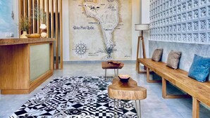 Un moderno vestíbulo de hotel con un mostrador de recepción de madera, un mural con un mapa, un suelo estampado y un área de descanso con una lámpara y cojines.