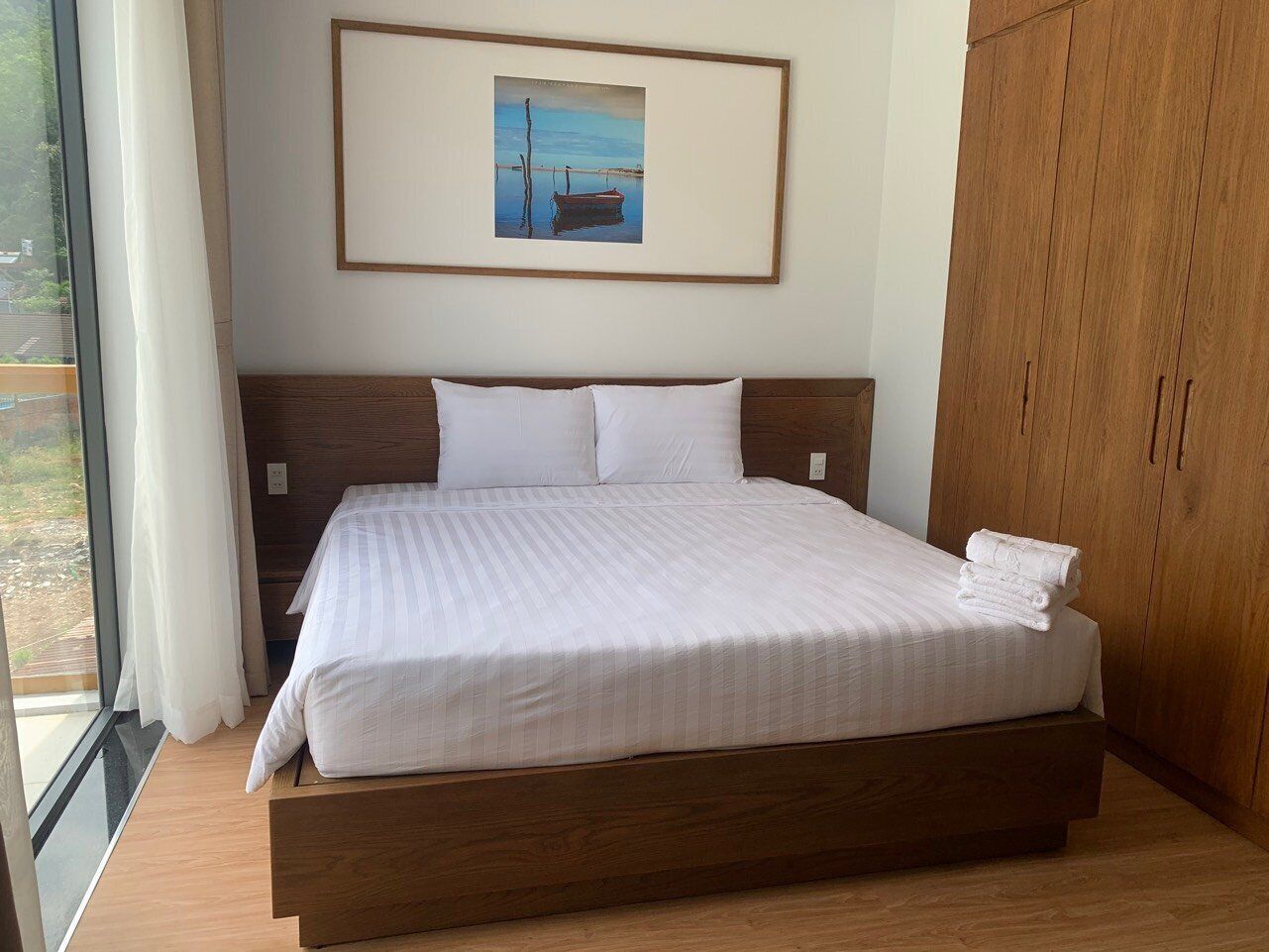 Una cama grande con cabecera de madera, ropa de cama blanca y un cuadro enmarcado encima.