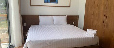 Una cama grande con cabecera de madera, ropa de cama blanca y un cuadro enmarcado encima.