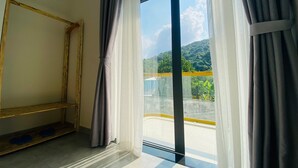 Una habitación con un ventanal grande, una silla de madera y vistas a un balcón y vegetación.