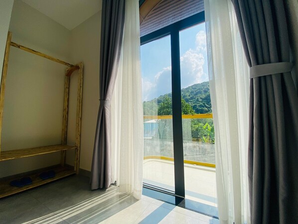Een kamer met een groot raam, een houten stoel en uitzicht op een balkon en groen.