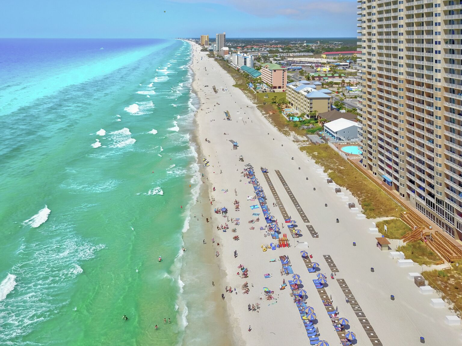 Ein Strand mit einer Reihe von Strandsonnenschirmen und Liegestühlen, ein Hochhaus und freie Sicht auf den Ozean.