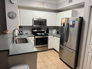 A modern kitchen with white cabinets, stainless steel appliances, a built-in microwave, and a refrigerator with safety stickers.