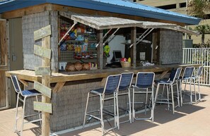 A small outdoor food stand with a wooden counter and metal chairs.