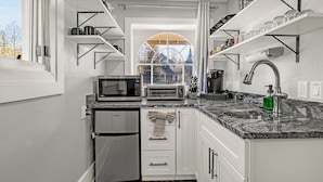 Una cocina moderna con armarios blancos, microondas integrado, refrigerador de acero inoxidable y encimera de granito.