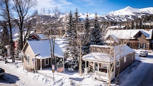 Un barrio residencial cubierto de nieve, con casas, una cabaña de madera y una montaña al fondo.