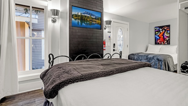 Un dormitorio con una cama grande, un televisor montado en una pared de ladrillo, un cuadro y una ventana con cortinas.