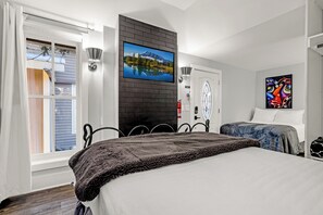 Une chambre à coucher avec un grand lit, un téléviseur fixé au mur en briques, un tableau et une fenêtre avec des rideaux.