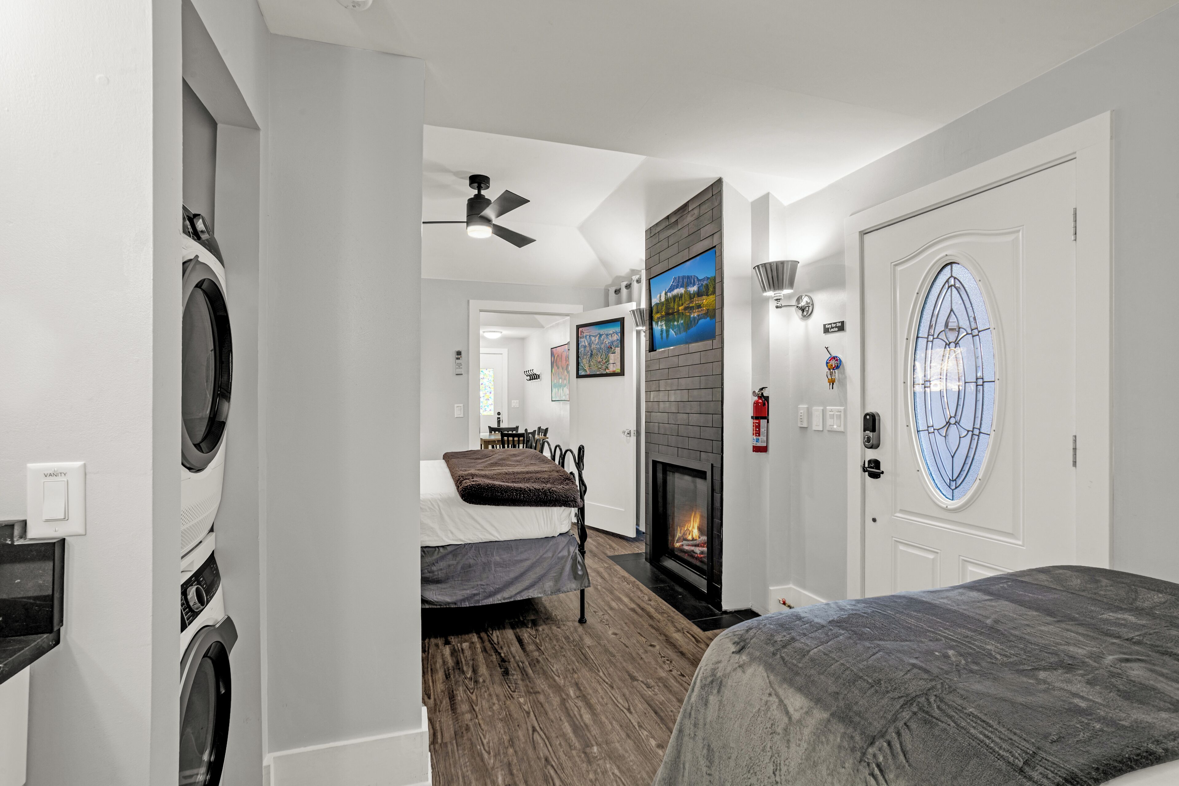 A hotel room with a fireplace, a bed, a second bed, a washing machine, and a door with a decorative glass panel.