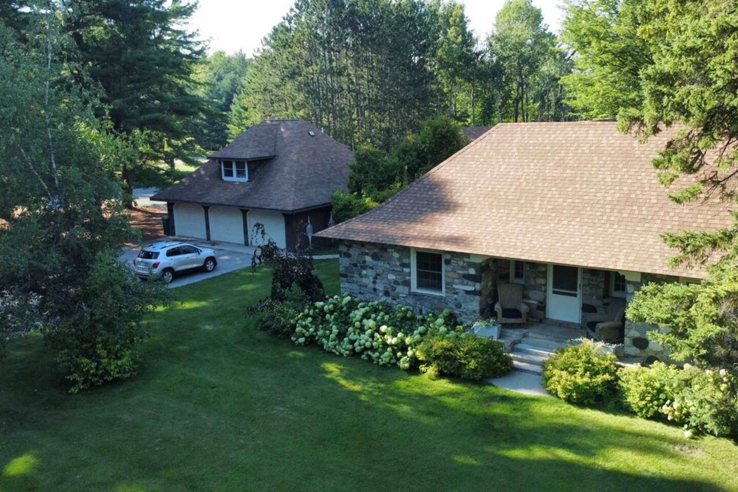 A two-story house with a stone exterior and a brick roof, surrounded by lush greenery and a well-maintained lawn.