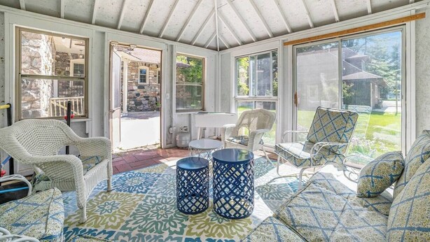 A sunroom with wicker furniture, a patterned rug, and a view of the outdoors. - Castle Farms Wedding Weekend Home (Charlevoix)