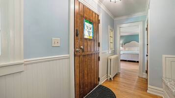 Un pasillo con una puerta de madera, un radiador y una cama en la habitación contigua.