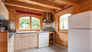 A kitchen with wooden walls, a stainless steel stove, and a white refrigerator. - Le Chamalo by Interhome (Saint Georges de la Rivière)