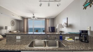 A modern kitchen with a granite countertop, a double sink, and a view of the ocean through large windows.