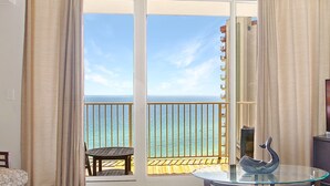 A balcony with a glass table and a decorative item, overlooking a clear blue sea and a building in the distance.