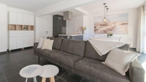 A modern living room with a grey sofa, two round tables, and a kitchen in the background. - Miramar with terrace by Interhome (Oostende)