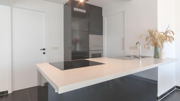 A modern kitchen with a central island, white cabinetry, and a black backsplash. - Miramar with terrace by Interhome (Oostende)
