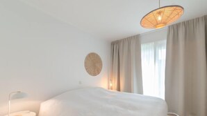 A modern bedroom with a large bed, a round wall decoration, a small table, and a hanging light fixture. - Miramar with terrace by Interhome (Oostende)