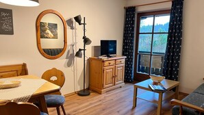 Een gezellige kamer met een houten eettafel, stoelen, een televisie en een raam met gordijnen.