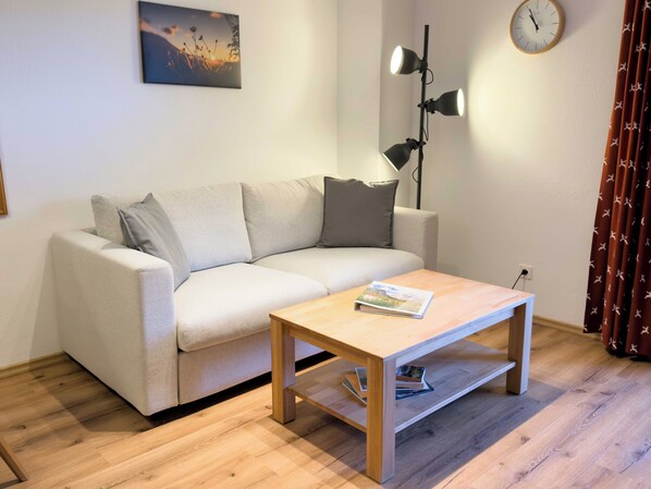 A living room with a sofa, a coffee table, a lamp, a clock, and a painting on the wall.