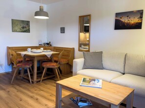 A dining area with a wooden table and chairs, a sofa, a small table with a book, and wall-mounted artwork.