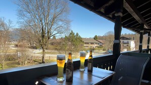 Un tavolo con un bicchiere di birra e bottiglie, una sedia e vista su edifici e alberi.