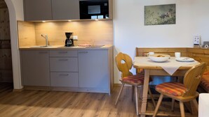 Una cucina funzionale con lavandino, macchina per caffè e pensili in legno. Si nota un tavolo con sedie e una lampada a sospensione.