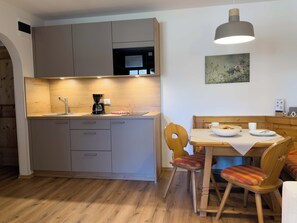 A compact kitchen with a sink, coffee maker, and wooden cabinets. There is a dining table with chairs and a hanging light fixture.