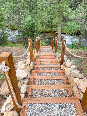 Un puente de madera con barandillas de cuerda que cruza un arroyo rocoso rodeado de follaje.