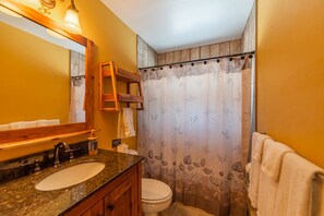 A bathroom with a granite countertop sink, a wooden vanity, a white toilet, and a shower curtain with a leaf pattern. - Private Creek & Trout Fishing - Mtn Views, 22 mi to Breckenridge (Fairplay)