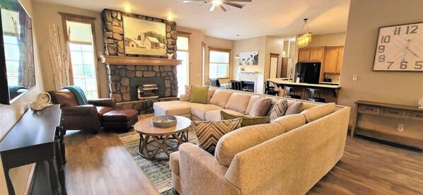 A spacious living room with a stone fireplace, a large sofa set, and a dining area with wooden cabinets.