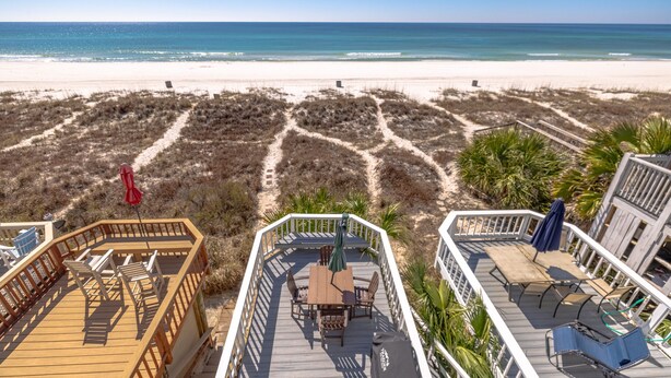 Une vue sur la plage avec une terrasse en bois, des sièges d’extérieur et une vue dégagée sur l’océan.